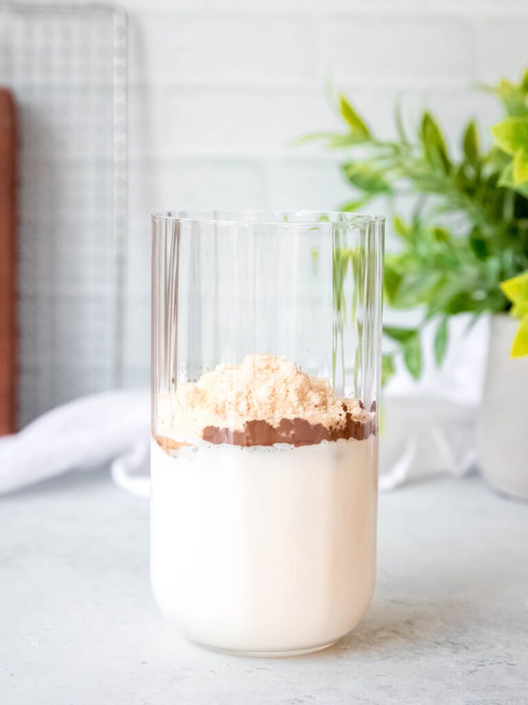 cream, milk, cocoa powder, and malted milk powder added to a glass to make chocolate cold foam.
