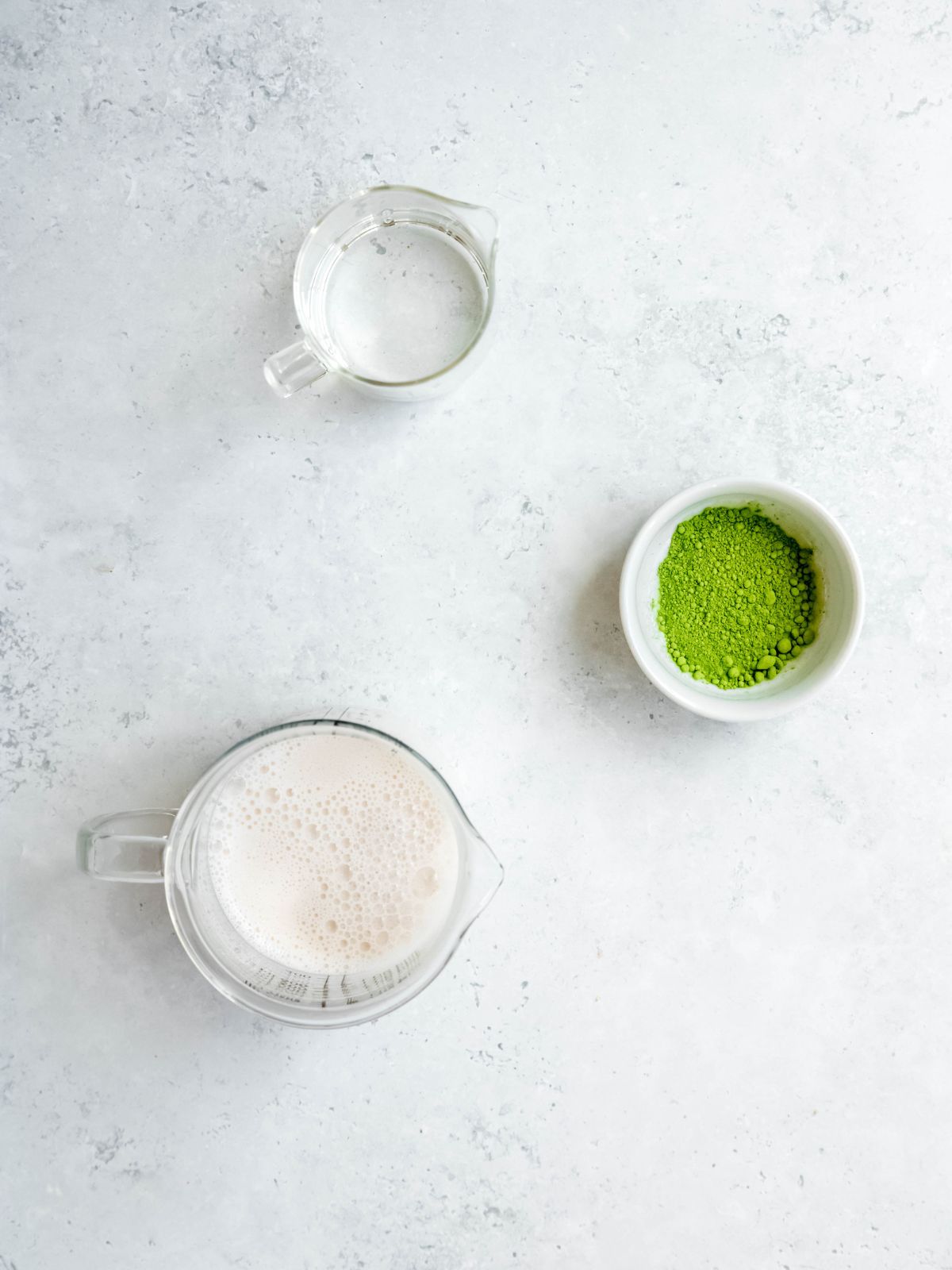 overhead shot of the ingredients needed to make a homemade starbucks copycat iced matcha latte on a white table.