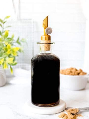 side on shot of a glass bottle with a stopper filled with dark brown sugar syrup.