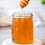 honey dipper drizzling honey into a glass jar.
