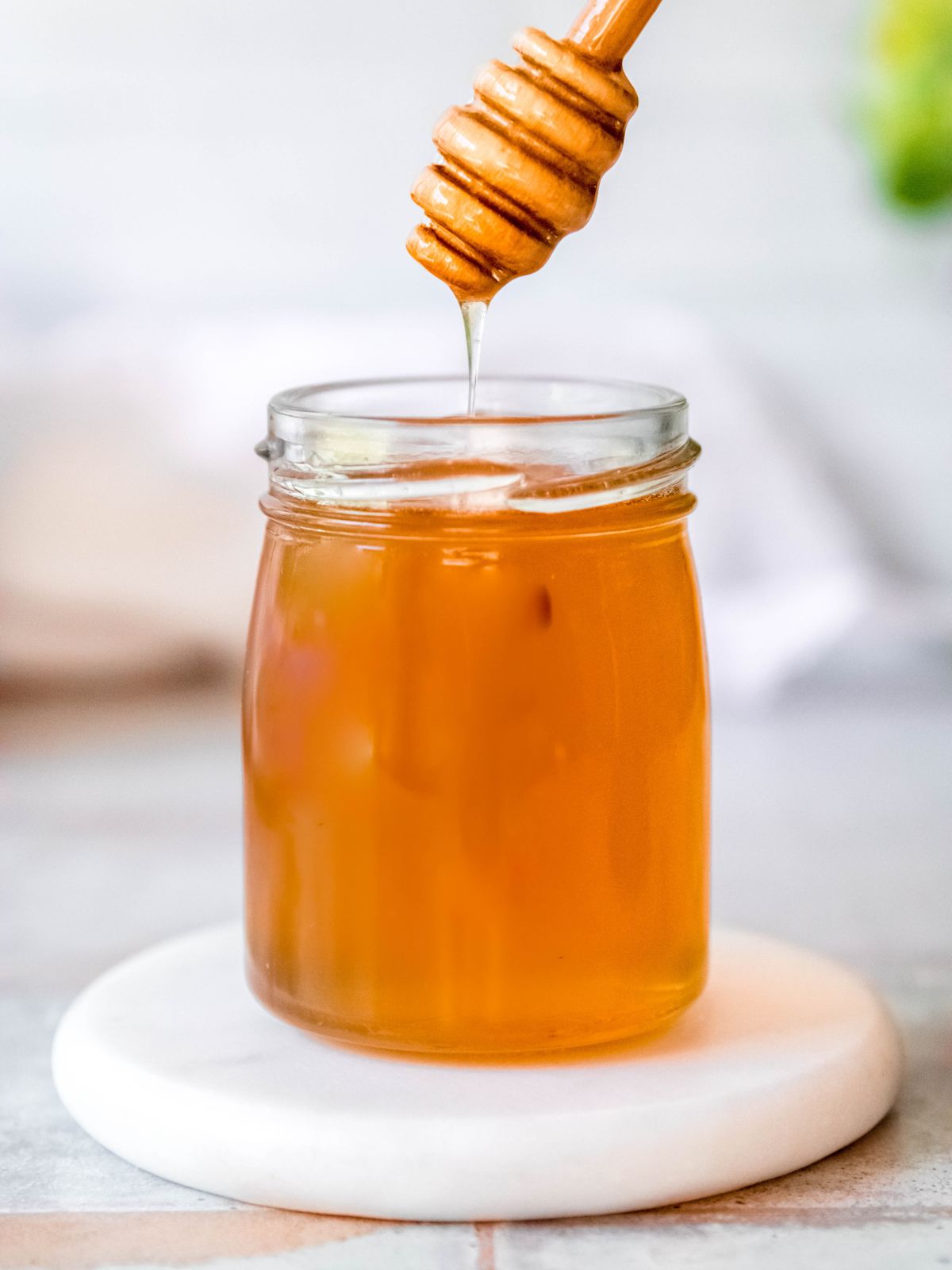 honey dipper drizzling honey into a small glass jar.