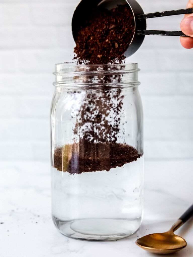 action shot of coarse coffee grounds being poured on top of water in the mason jar.