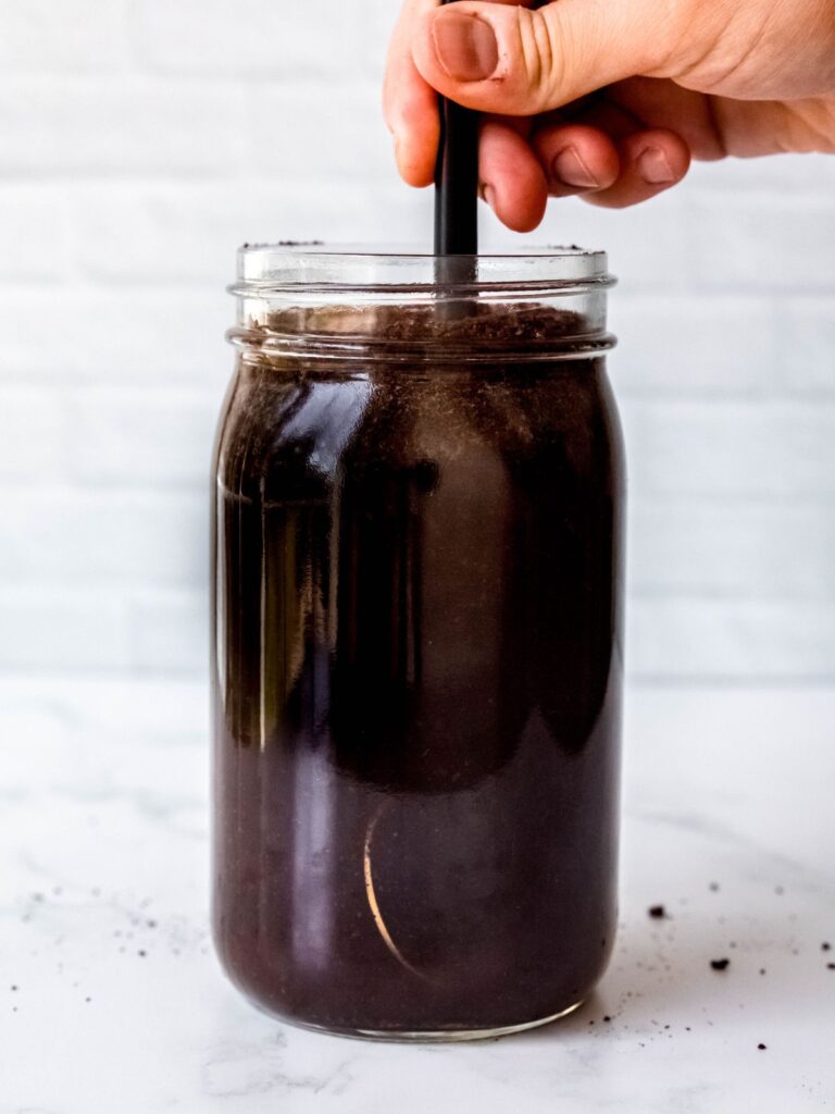 hand stirring together the coffee grounds and cool water to make homemade cold brew.