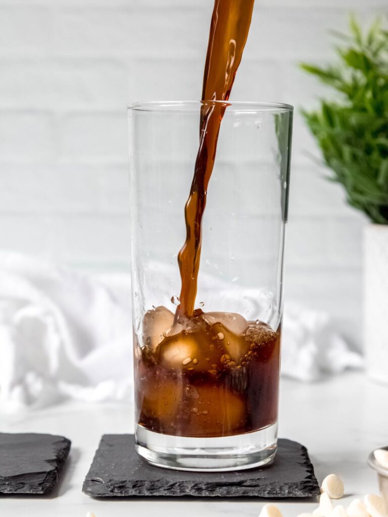 action shot of cold brew coffee being poured into a glass of ice.