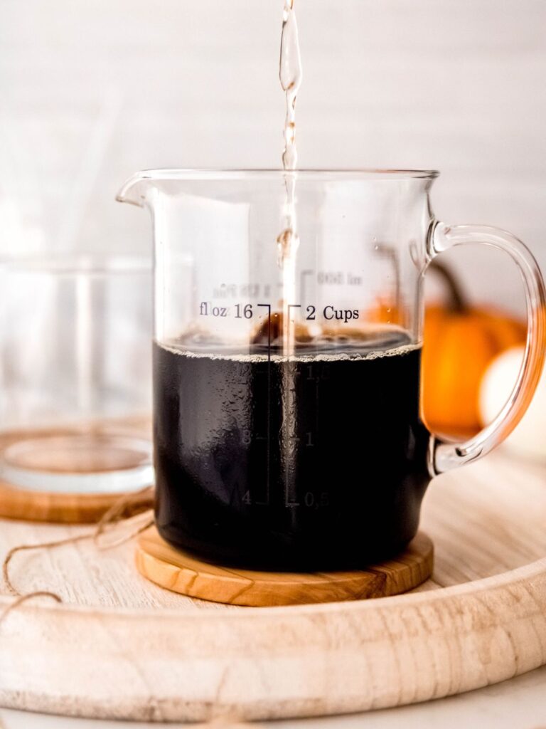 action shot of vanilla syrup being poured into a glass measuring cup with cold brew coffee.