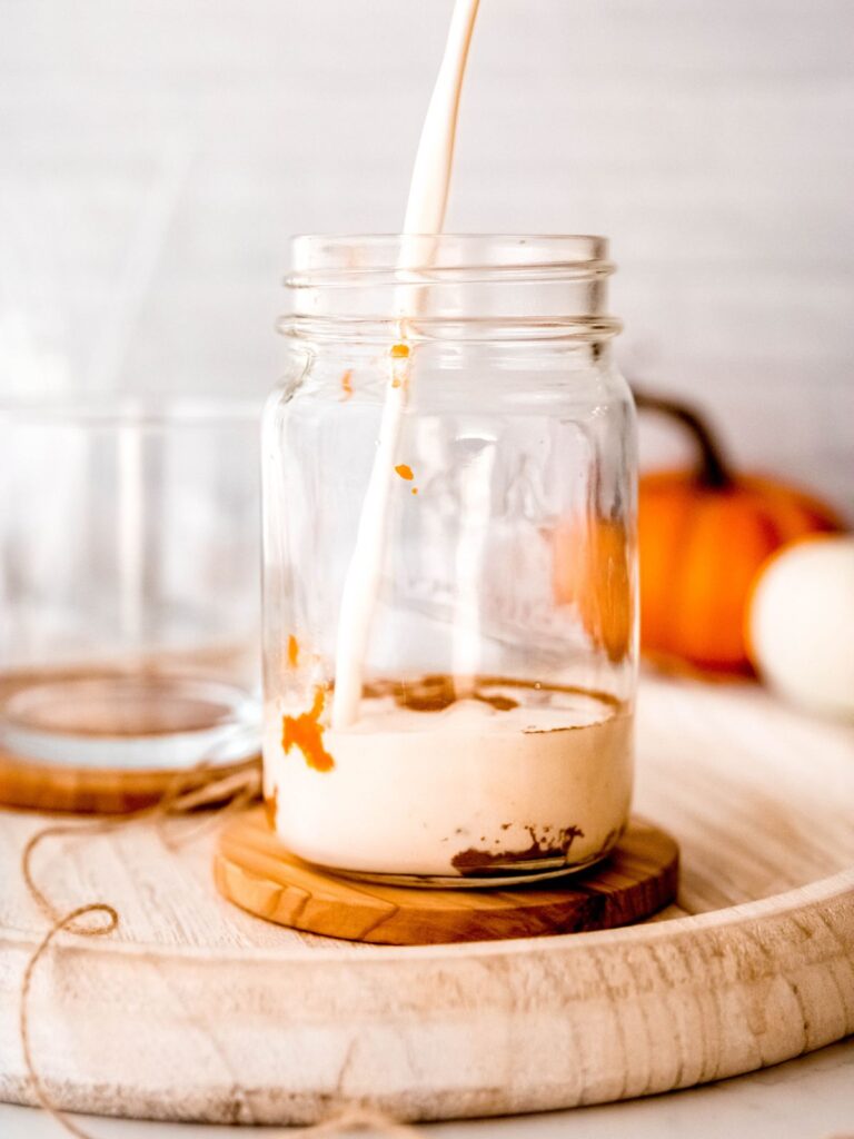action shot of cream being poured in a mason jar with pumpkin puree.