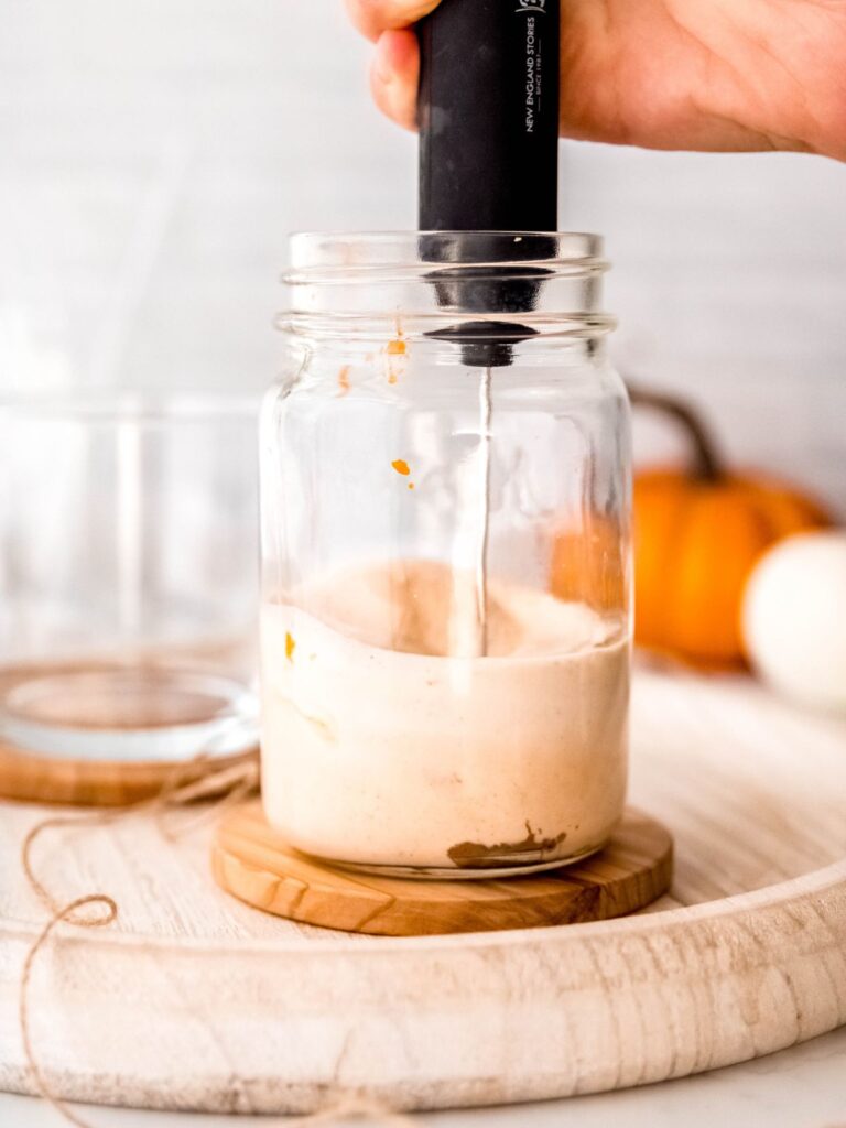 action shot of a handheld frother making pumpkin cream cold foam in the mason jar.