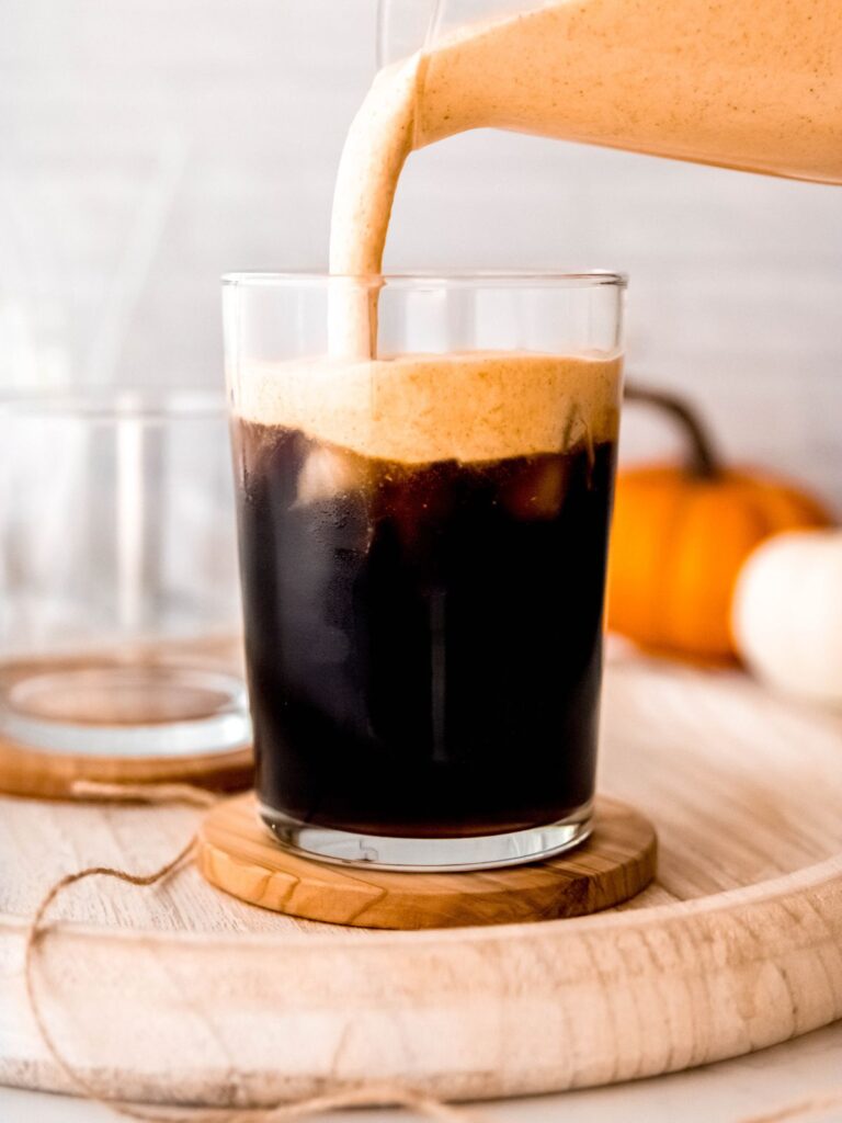 action shot of pumpkin cream cold foam being poured on top of a glass of lightly sweetened cold brew.
