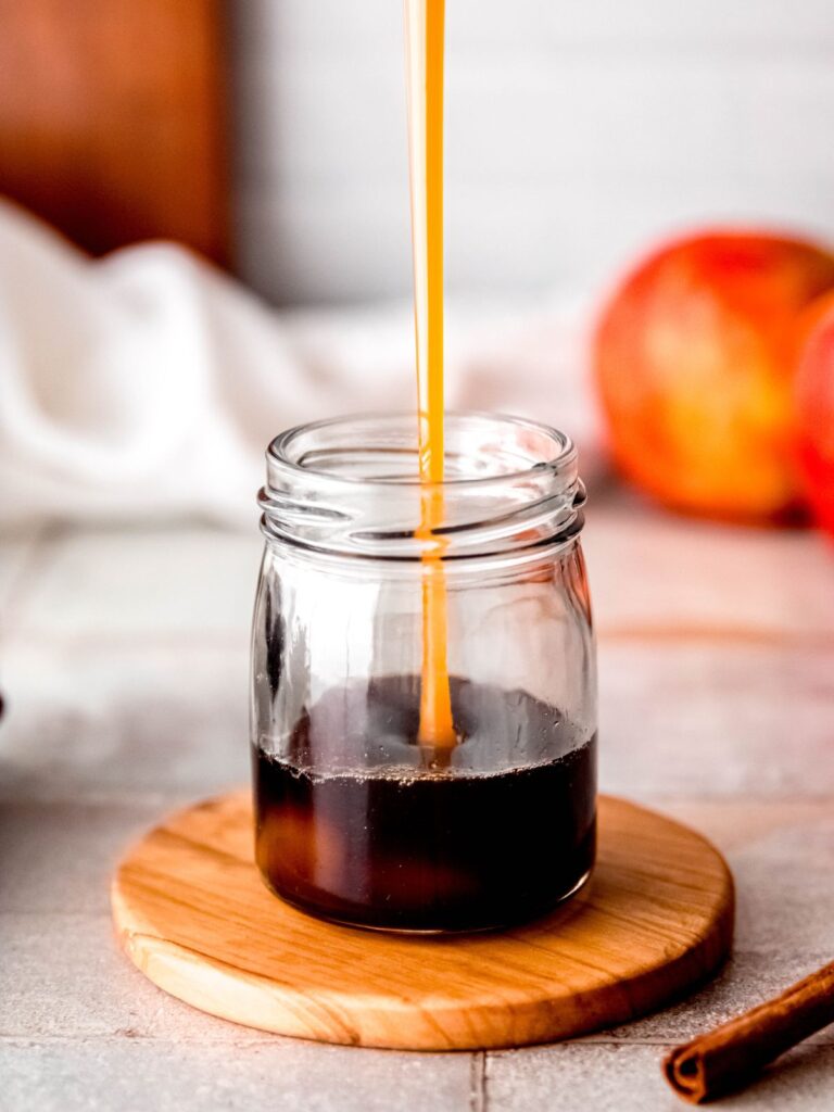 action shot of pouring caramel sauce into a jar with the apple brown sugar syrup.