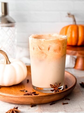 wooden try with a glass of iced pumpkin cream chai latte with whole star anise and a mini white pumpkin.