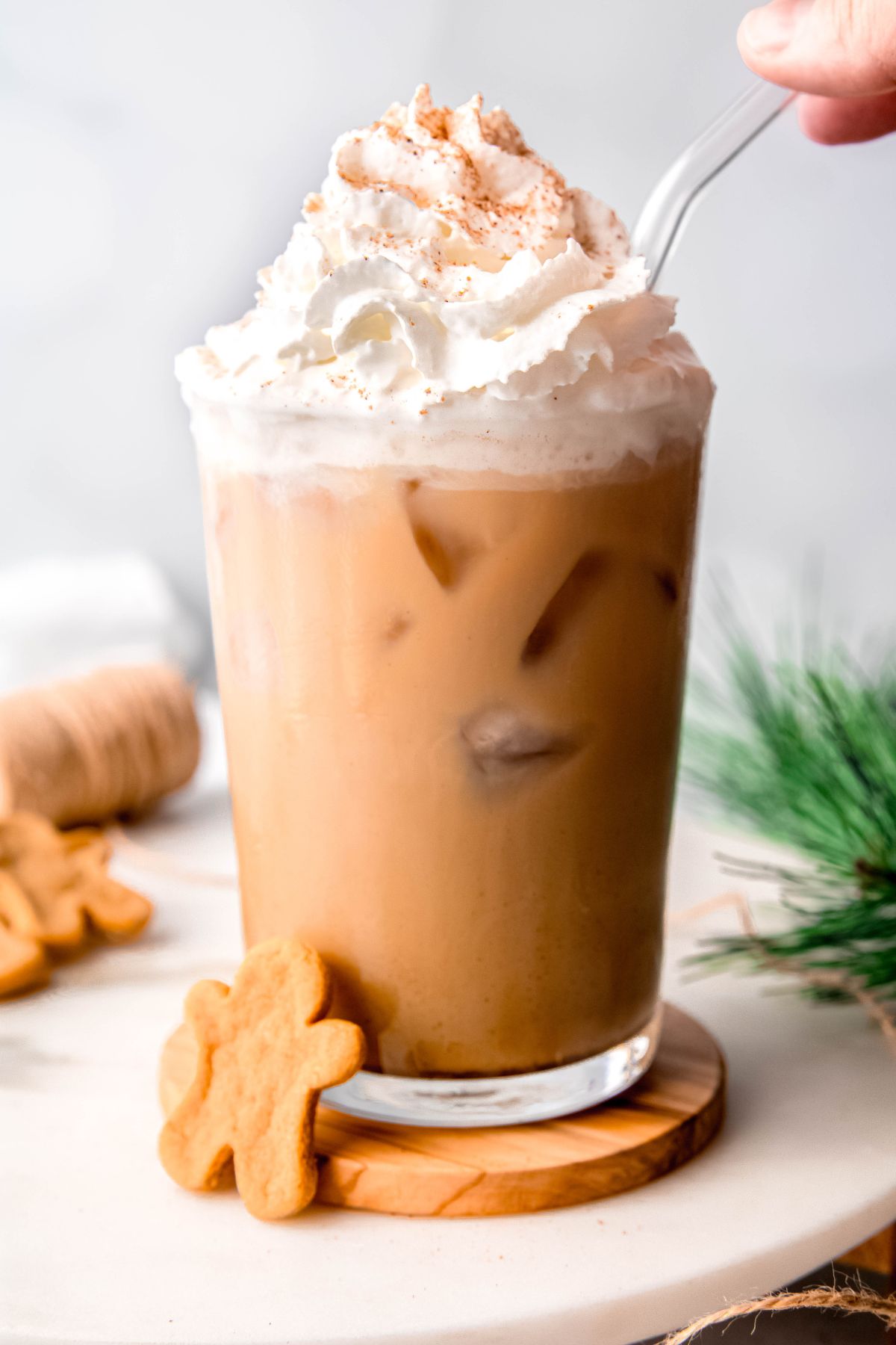 Adding a clear straw to a glass of iced gingerbread chai latte with whipped cream.