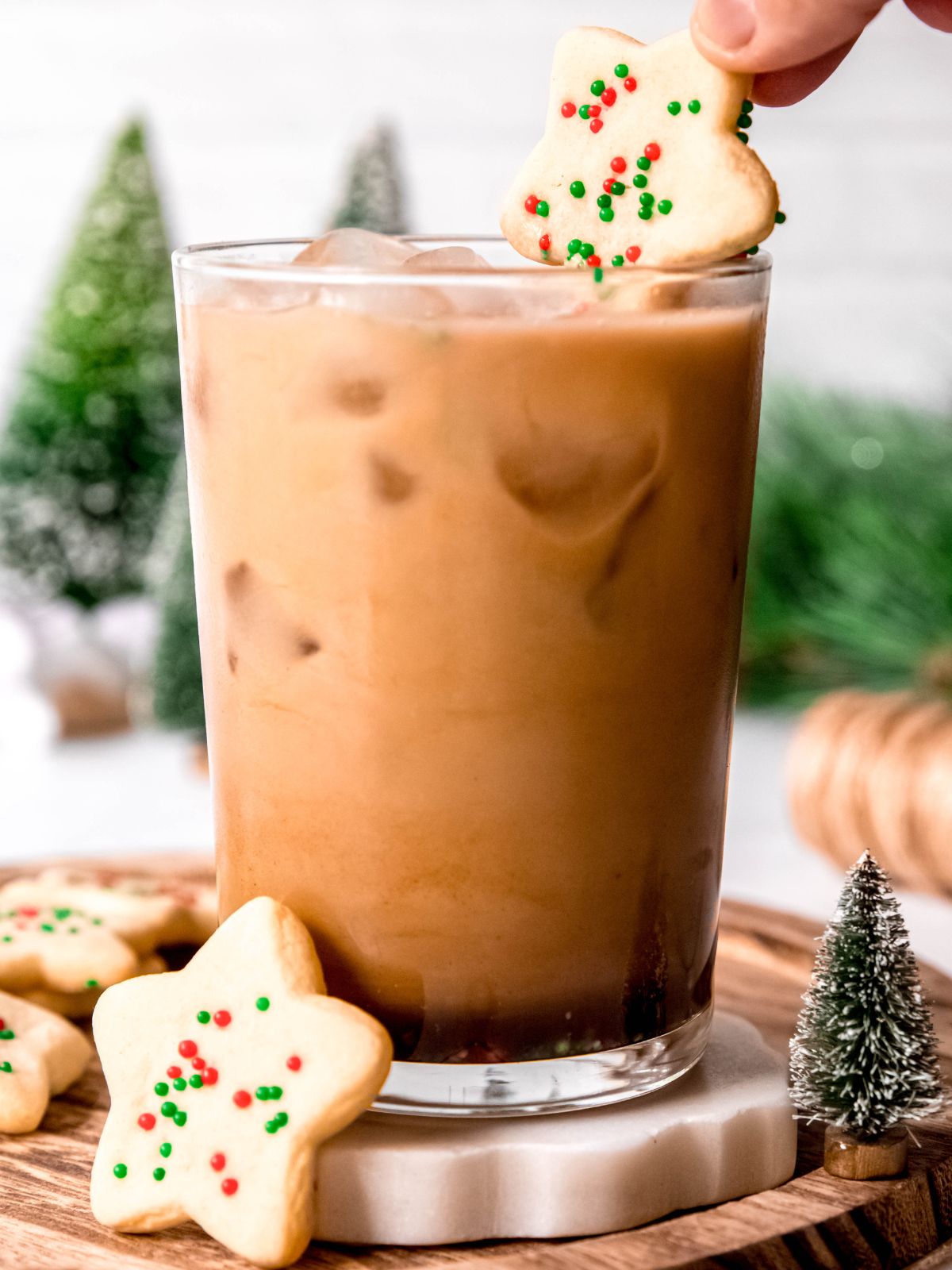 hand holding a sugar cookie dipping it into the sugar cookie almond milk iced latte.