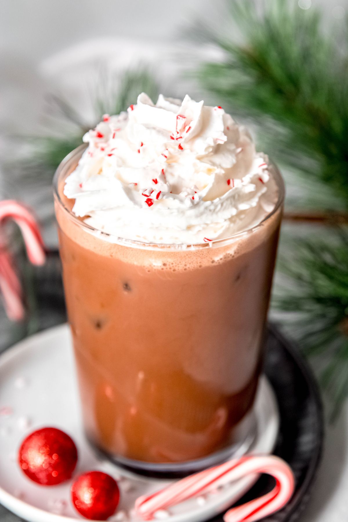 45 degree angle shot of a clear glass with an iced peppermint mocha topped with whipped cream and crushed candy canes.