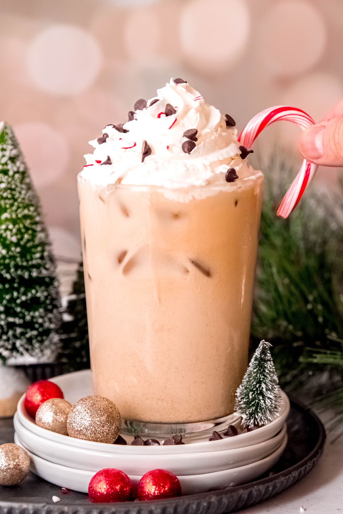 hand dipping a mini candy cane into a glass of iced peppermint white mocha.