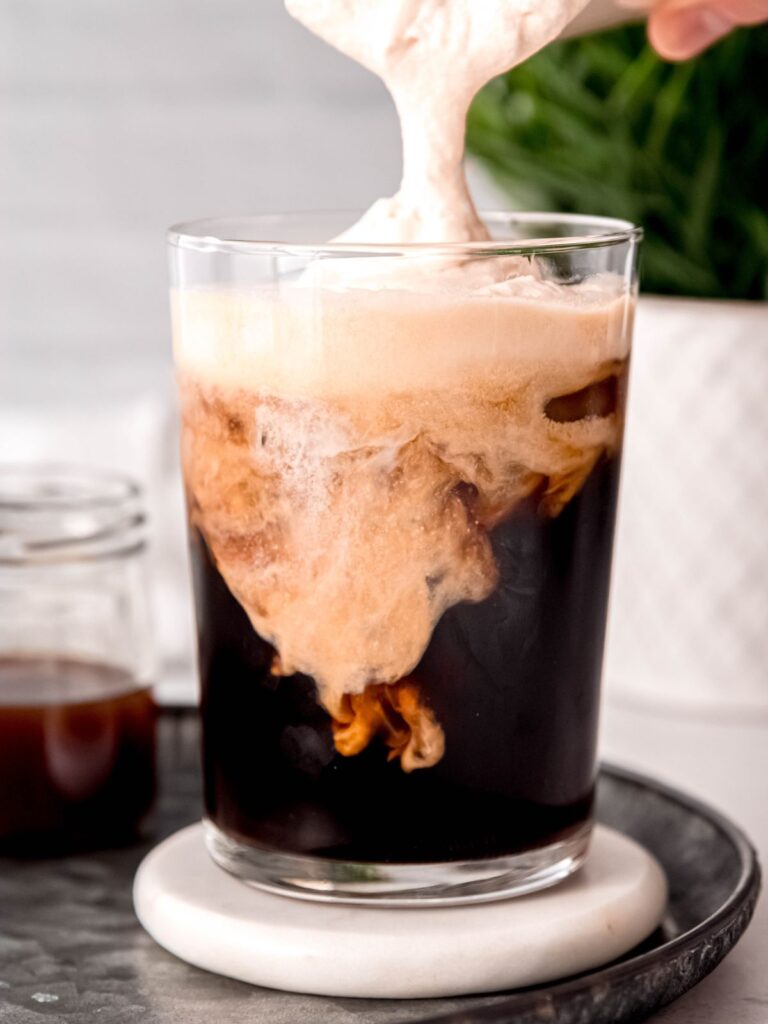 Pouring the cold foam onto the glass of cold brew.