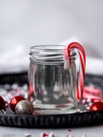 black tray filled with mini red and silver ornaments and crushed candy canes with a jar of peppermint simple syrup in the middle.
