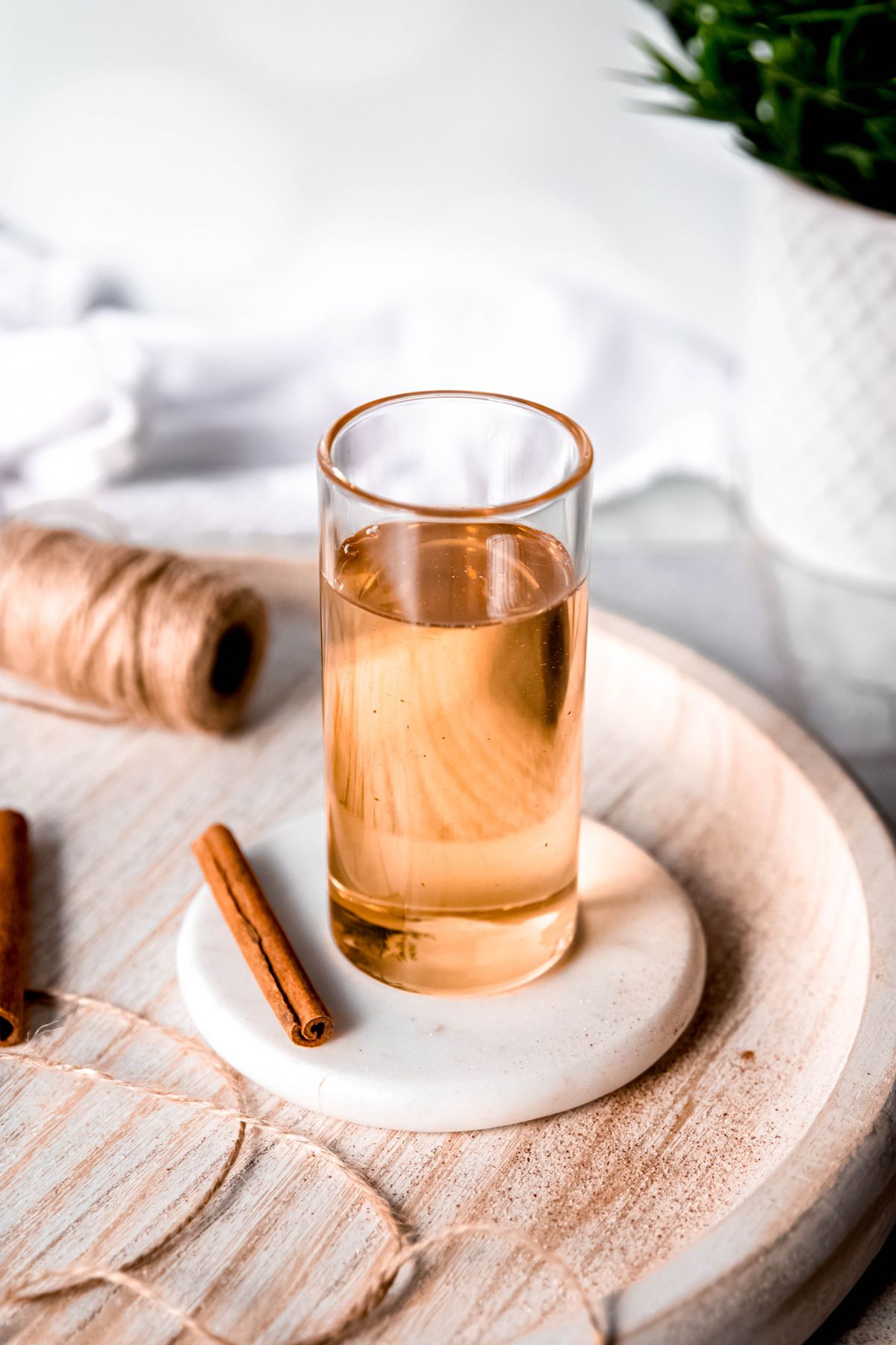 glass of cinnamon syrup on a white coaster with a stick of canela.