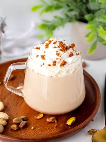 hero shot of homemade starbucks pistachio latte on a table with a plant and a golden spoon.