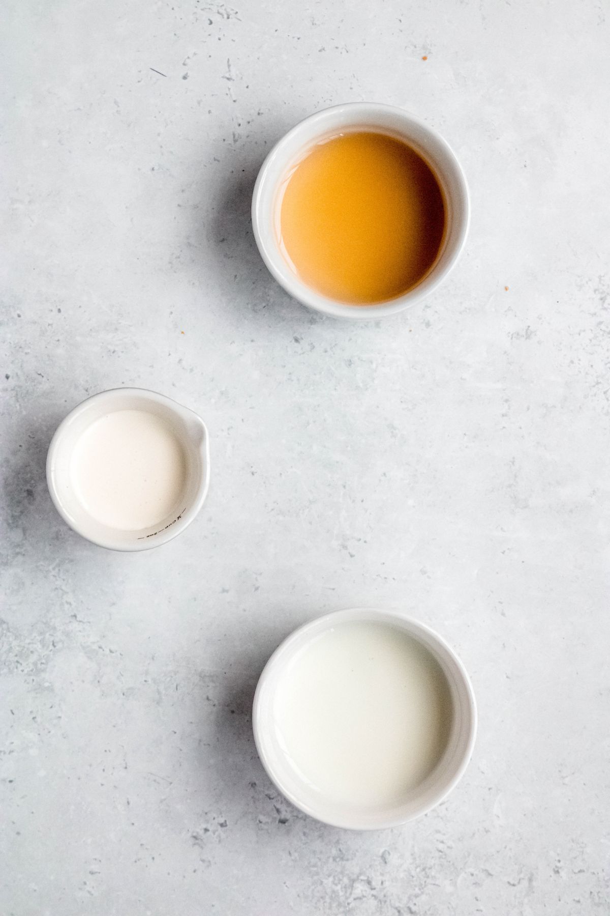 flat lay shot of the ingredients needed to make sweet cream cold foam measured out into bowls on a white table.