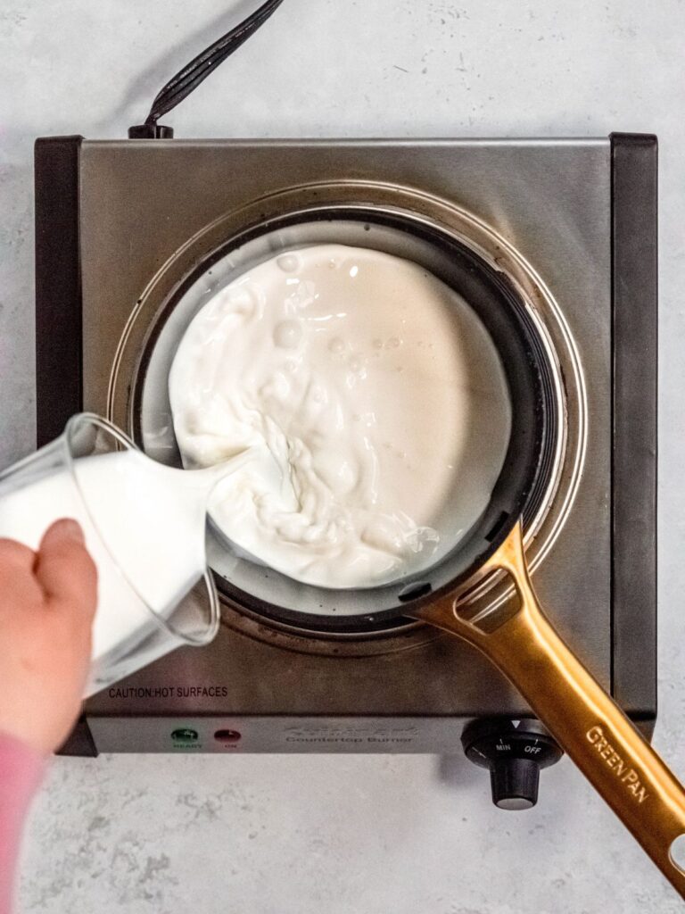 Pouring the half and half and cream into a pot on the burner.