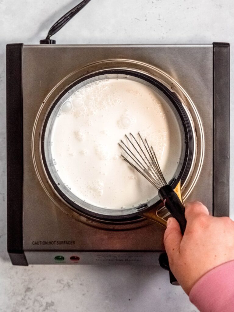 Overhead shot of a hand whisking a pot of half and half and cream.