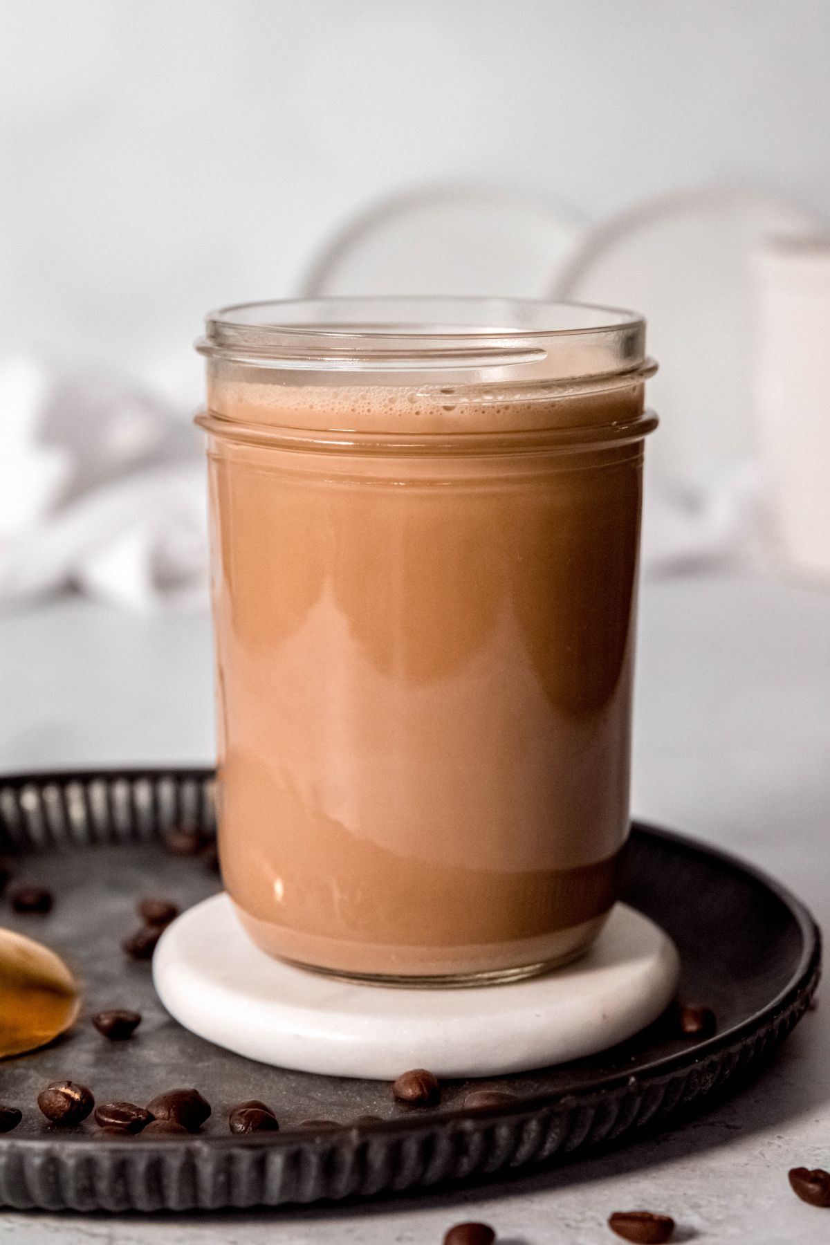 A side shot of a glass jar of Irish Cream homemade coffee creamer on a metal tray with coffee beans.