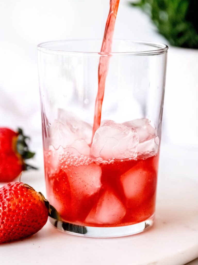 action shot of pouring the strawberry acai refresher base over ice. 