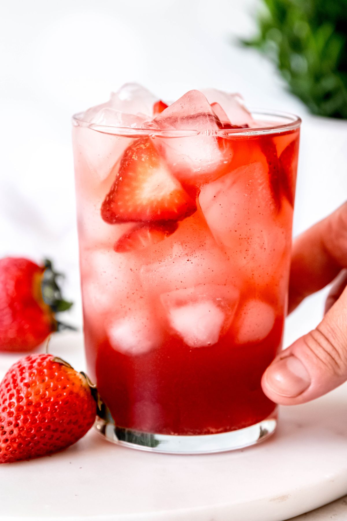 hand grabbing a clear glass of a homemade strawberry acail refresher starbucks copycat.