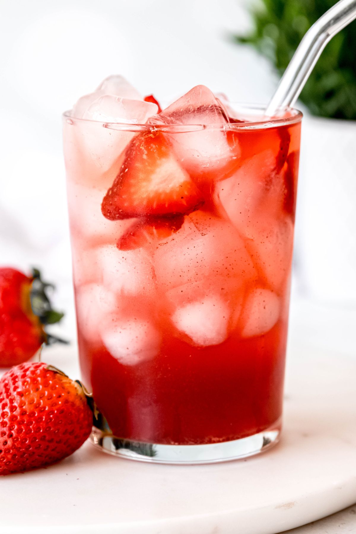 clear pint glass filled with a homemade strawberry acai refresher garnished with fresh strawberry slices and a glass straw.