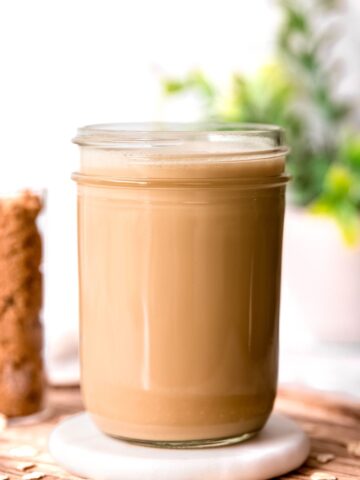 An up-close side shot of a large glass of brown sugar oat milk creamer on a coaster.