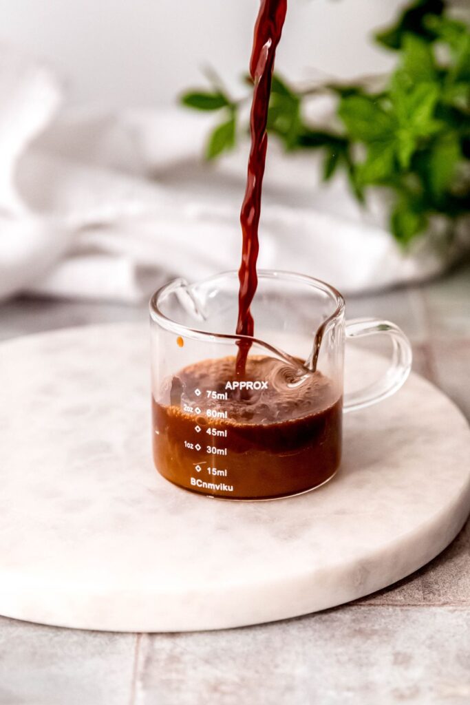 Pouring espresso into a small glass with the flavored syrup. 