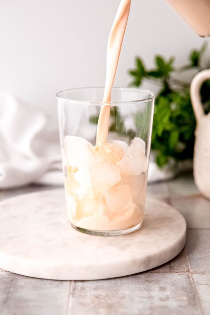 Pouring a protein shake into a tall glass with ice. 