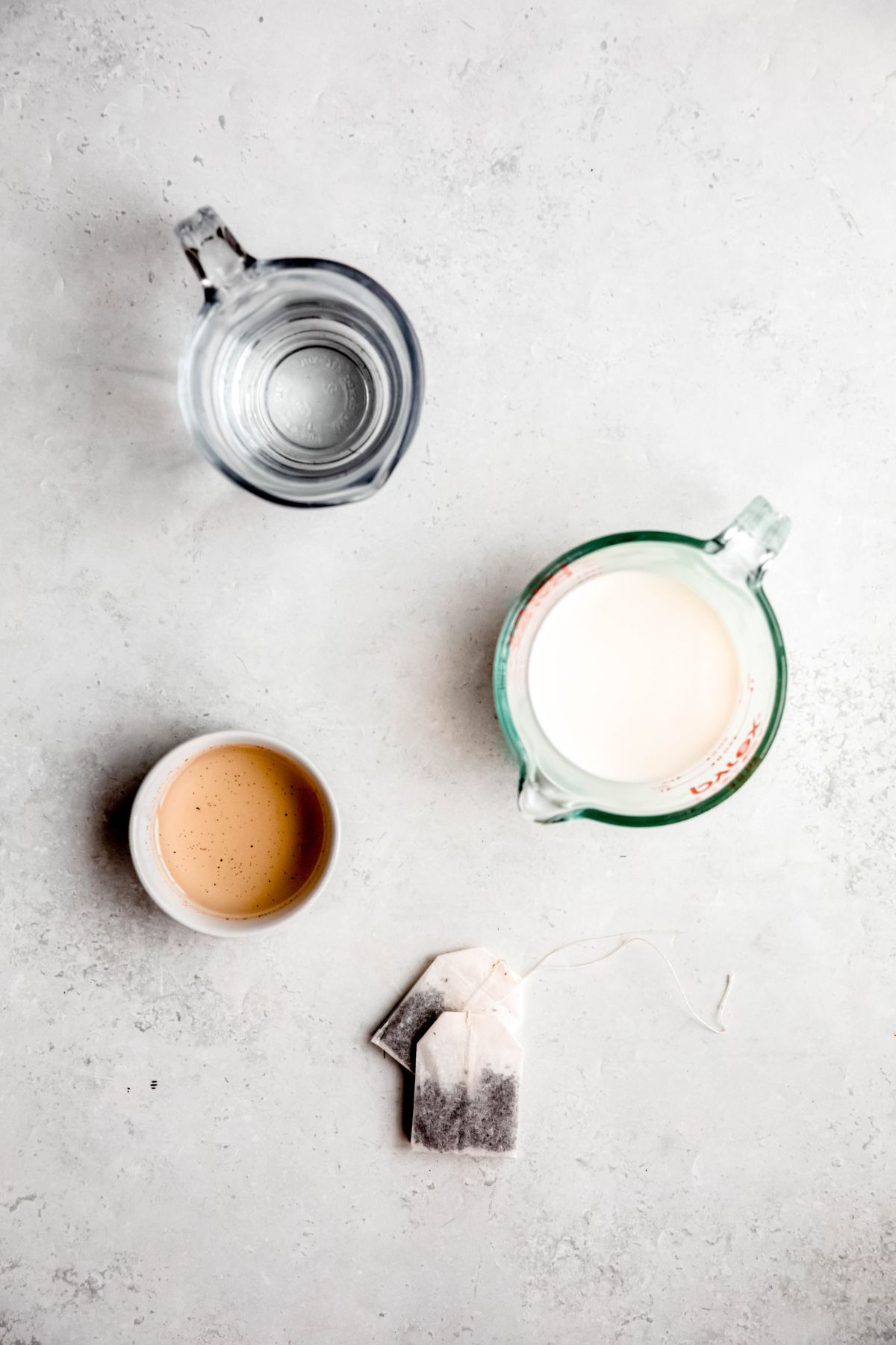 earl grey tea bags, milk, toasted vanilla syrup and hot water measured out on a white table for making copycat Starbucks london fog recipe. 