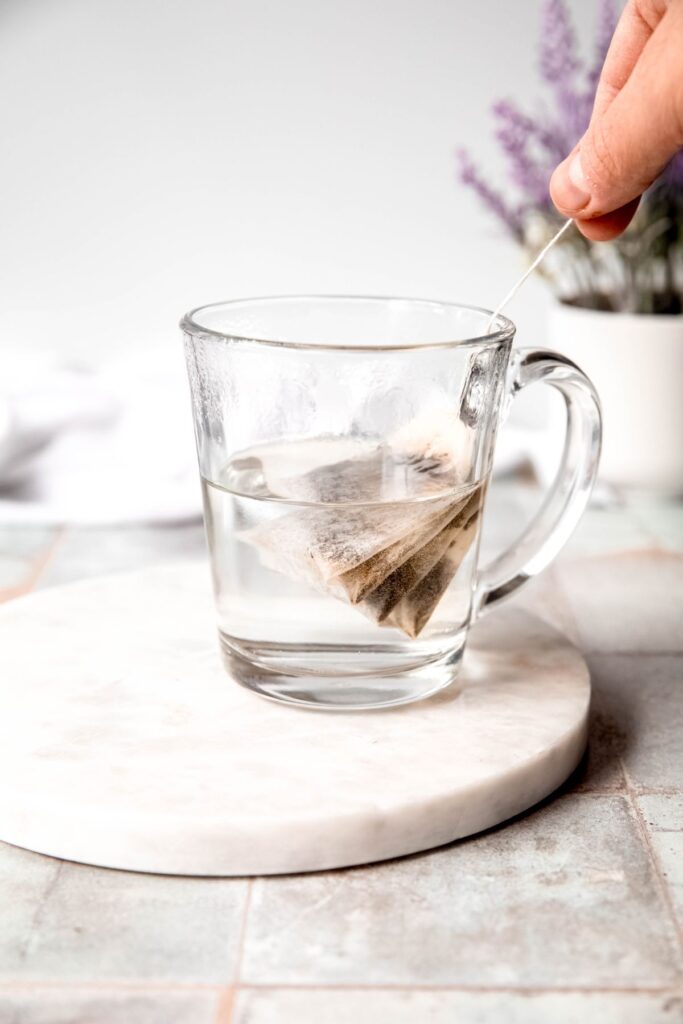 hand dunking the tea bags into hot water in a clear mug. 