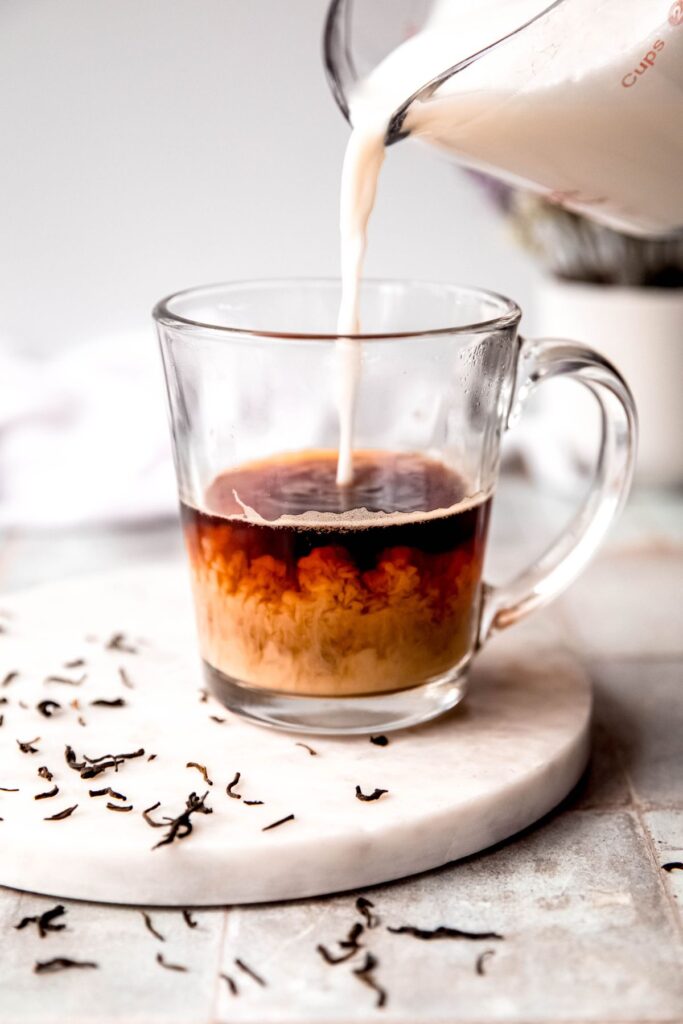 action shot of sweetened frothed milk being poured into the mug with the strongly brewed tea. 
