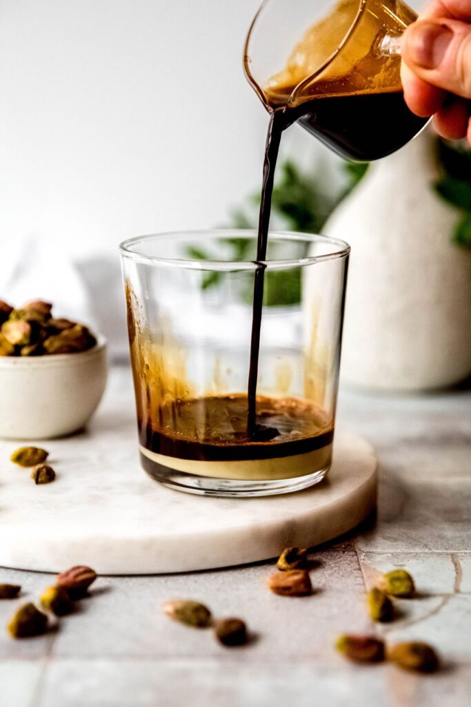 espresso being poured into a clear glass with the pistachio sauce in it. 