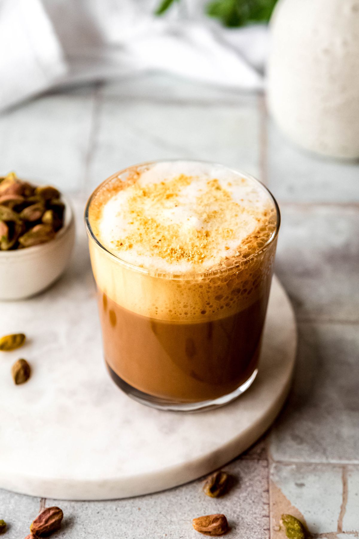 closeup 45 degree angle shot of a biscoff topped pistachio cortado made with frothed oat milk. 