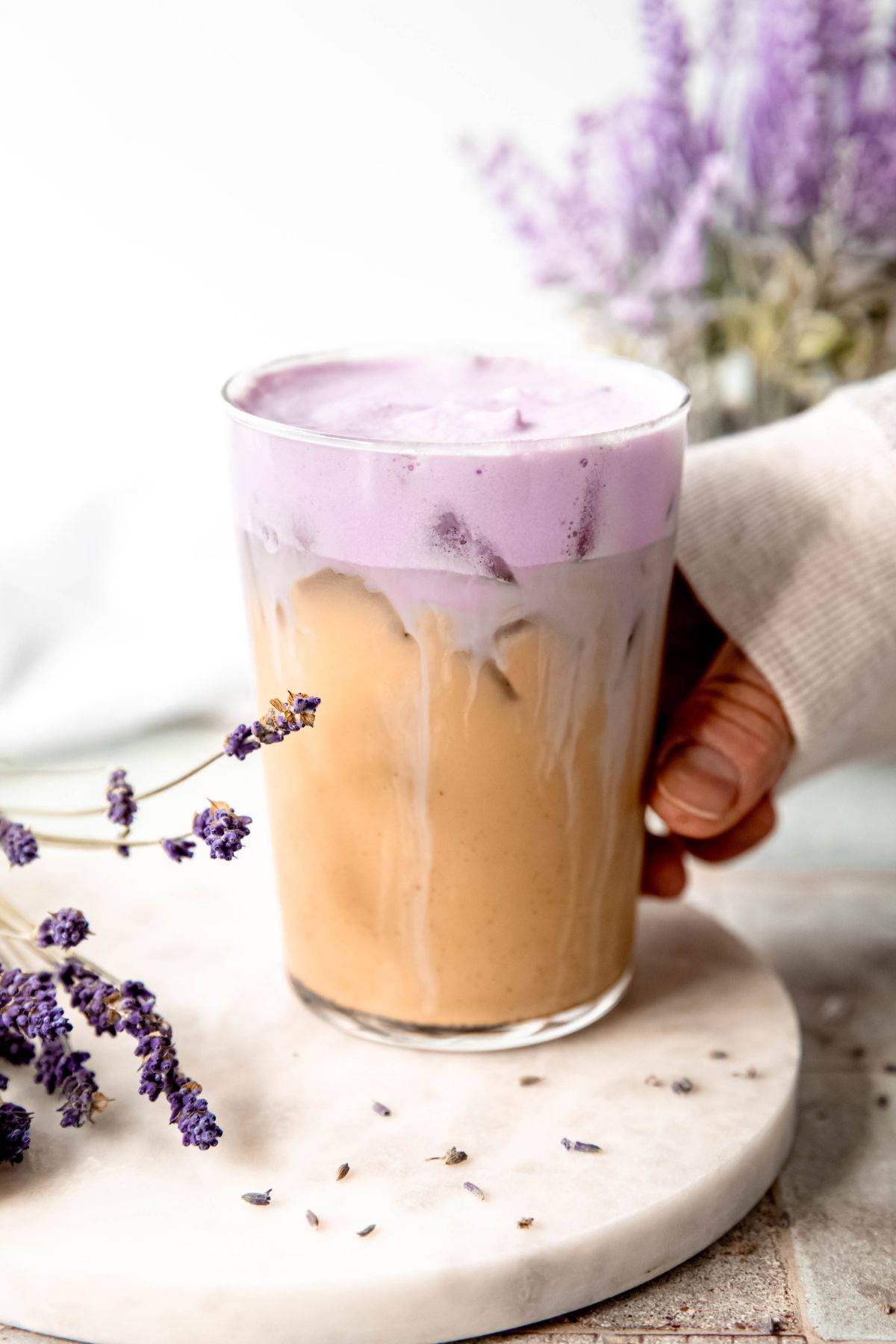 A side shot of a hand grabbing a tall glass of Iced Lavender Cream Chai. 