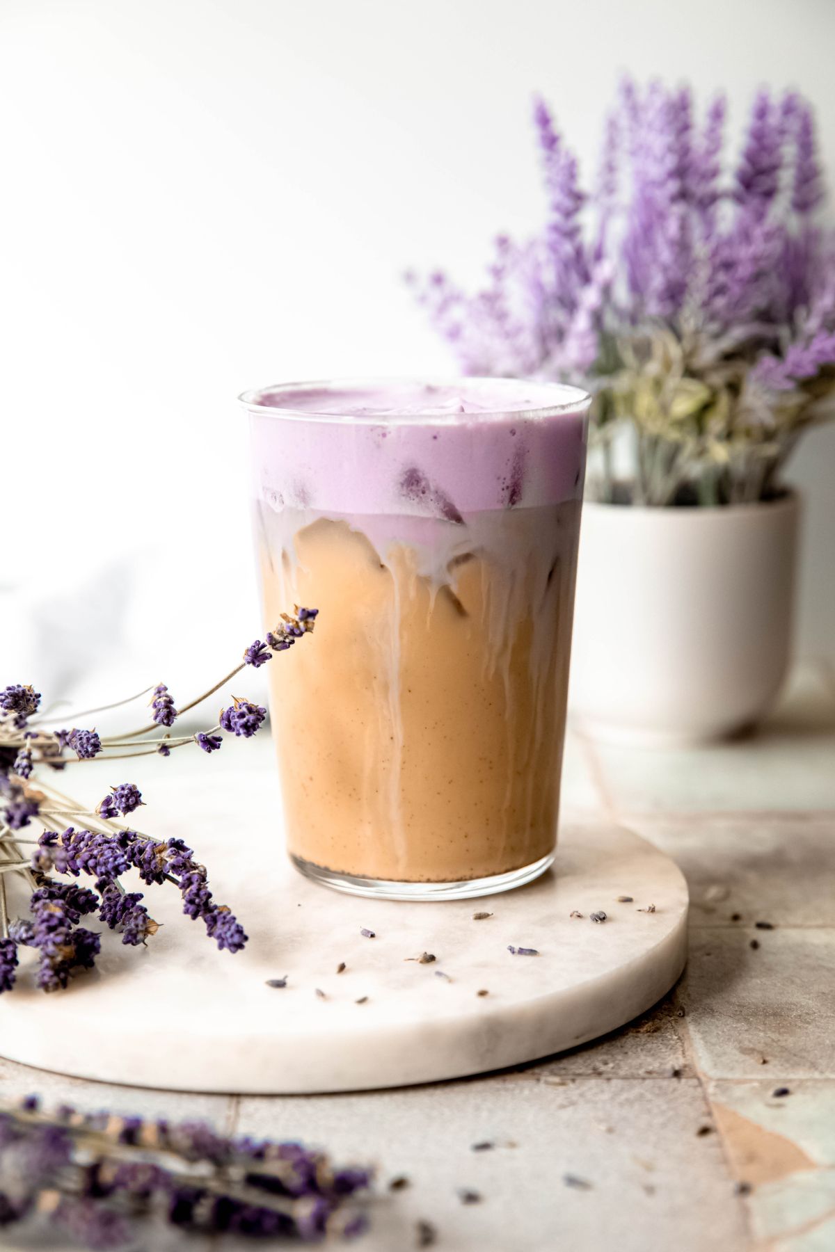 A side shot of a glass of Iced Lavender Cream Chai on the counter with fresh and dried lavender. 