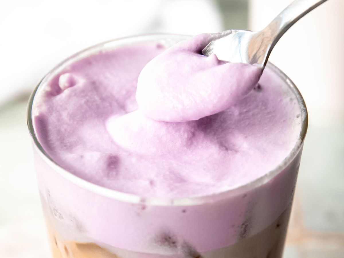 closeup horizontally framed hero shot of a silver spoon dolloping lavender cream cold foam on an iced drink. 