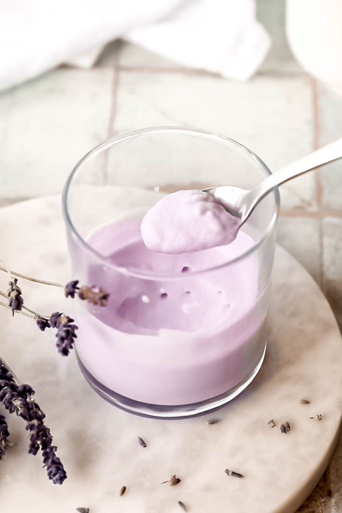45 degree overhead shot of a silver spoon taking some homemade lavender cream cold foam from the glass after frothing. 