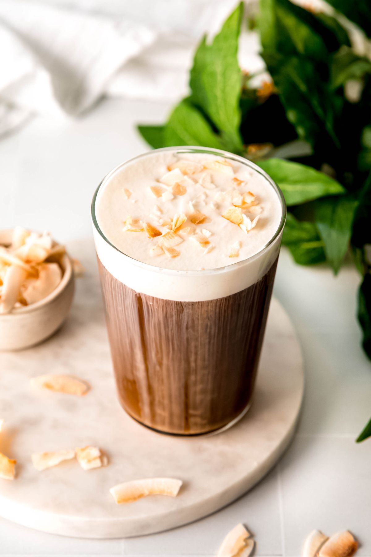 An up-close angled shot of a tall glass of coconut cream cold brew topped with toasted coconut. 