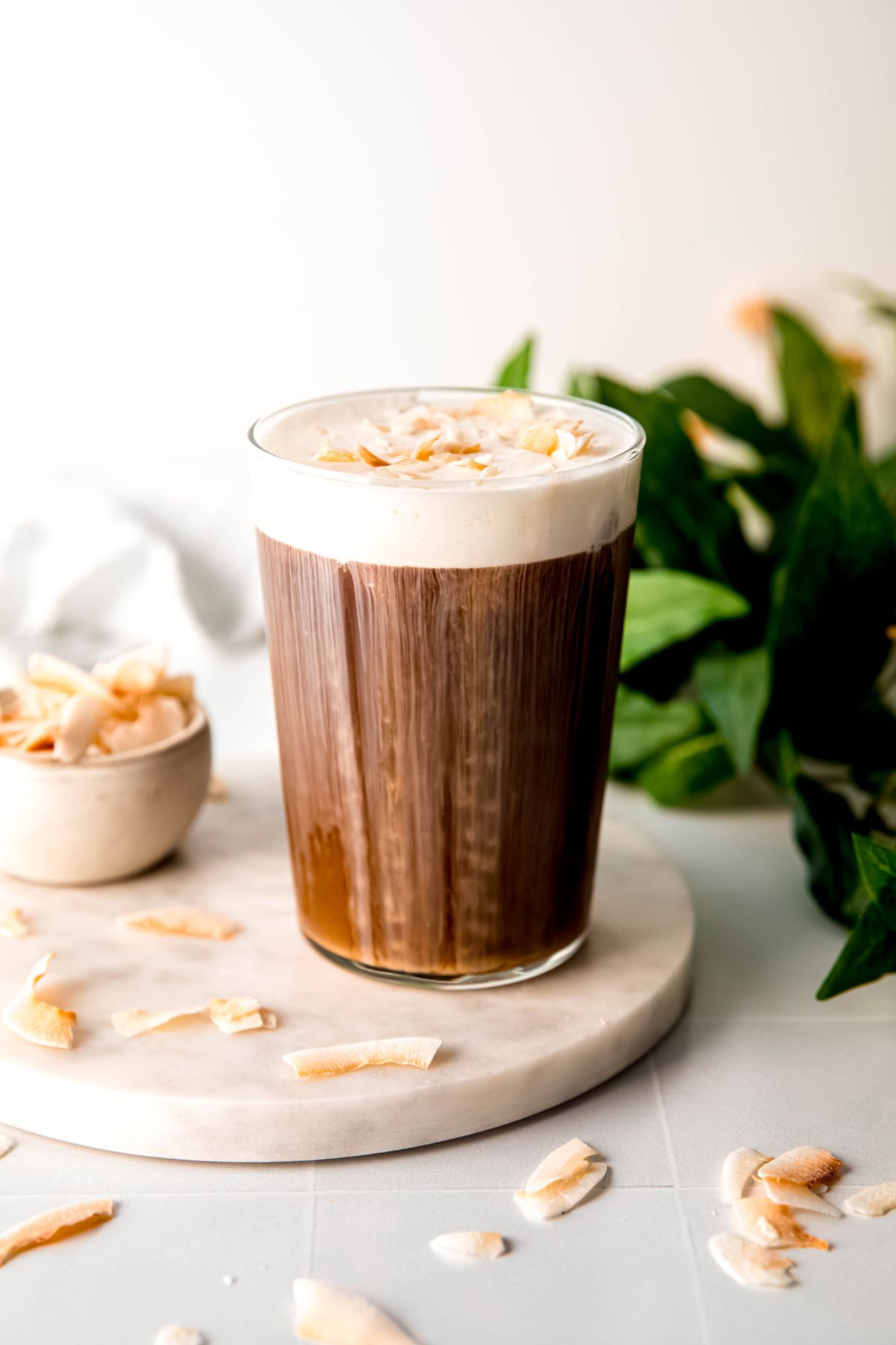 A side shot of a glass of coconut cream cold brew on the counter with toasted coconut chips. 