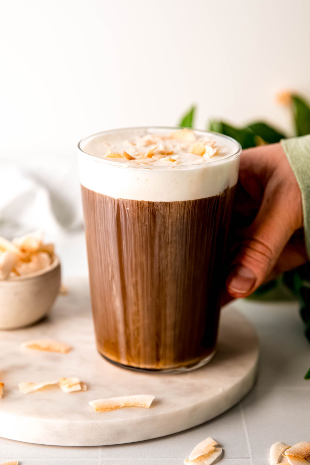 A hand grabbing a tall glass of coconut cream cold brew from the counter. 