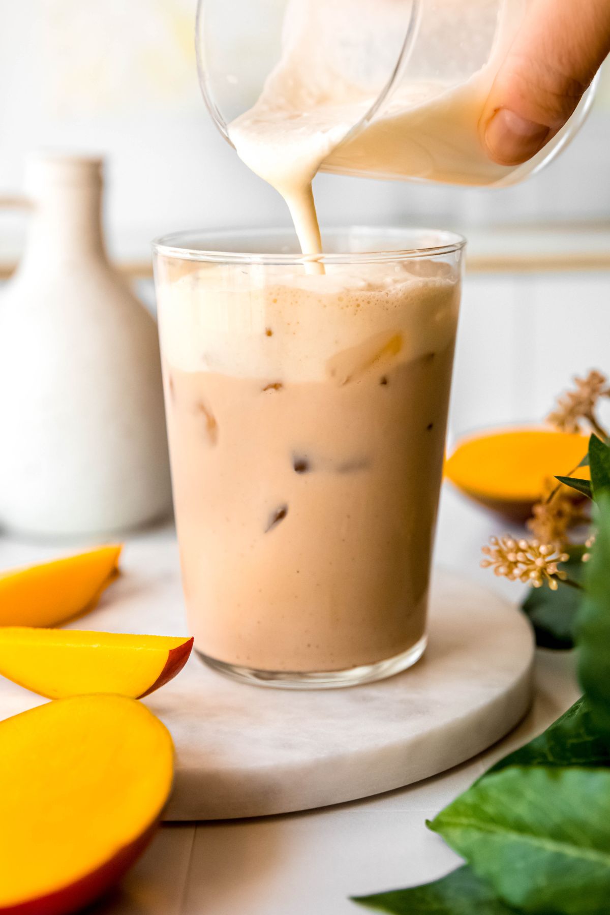 action shot of mango cream cold foam being poured onto the iced chai latte. 
