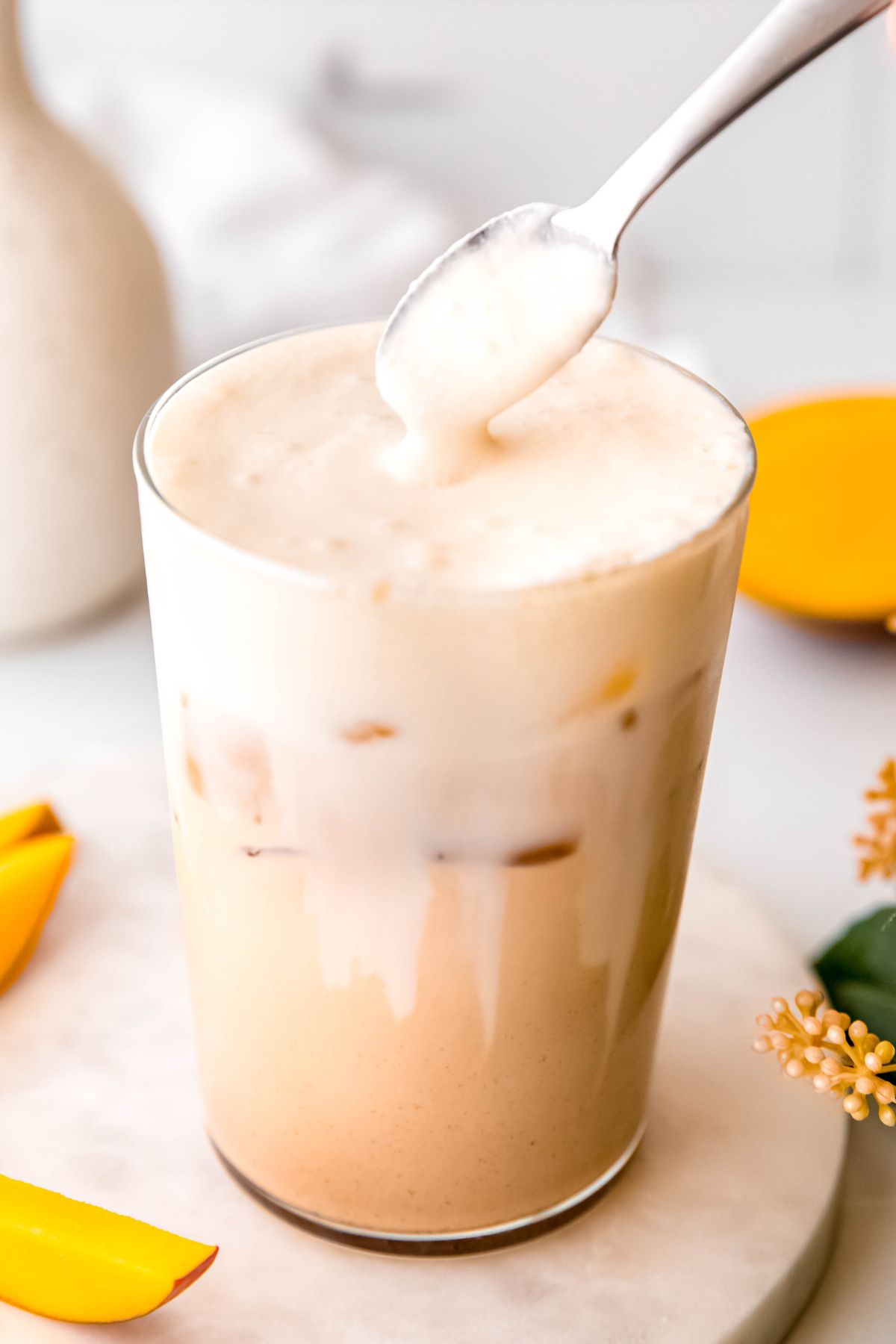 action shot of a silver spoon dolloping mango cream cold foam on top of an iced chai latte.