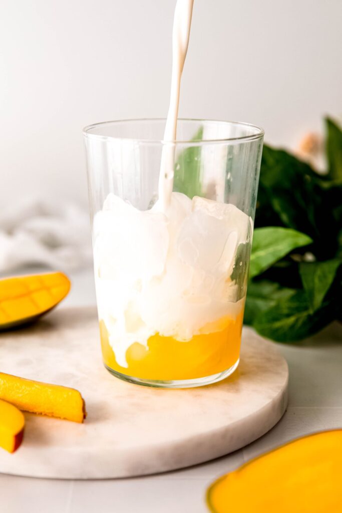 action shot of milk being poured into a glass of ice with mango syrup. 