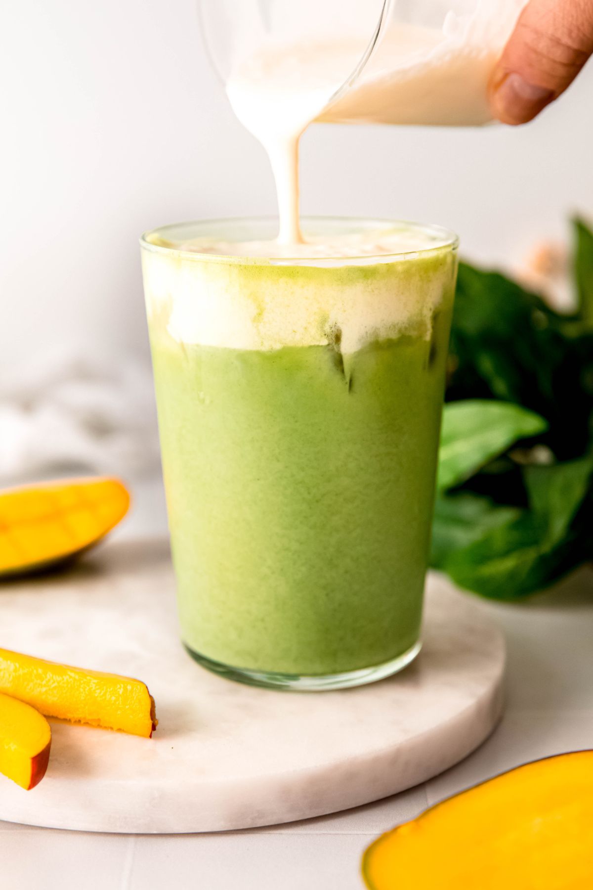 action shot of a hand pouring mango cream cold foam on the mixed iced matcha latte below. 