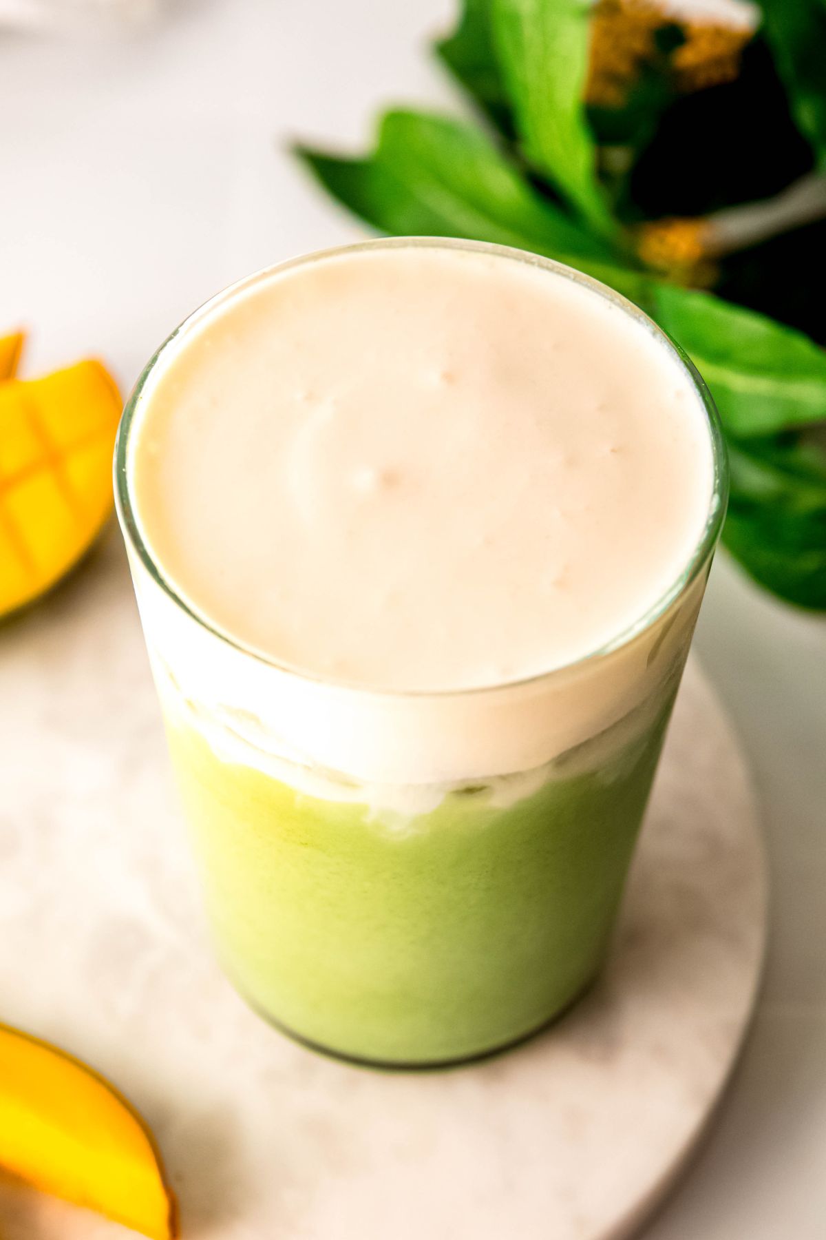 45 degree overhead shot of a starbucks copycat iced mango cream matcha latte showing the creamy mango foam top resting on a pale green matcha base. 