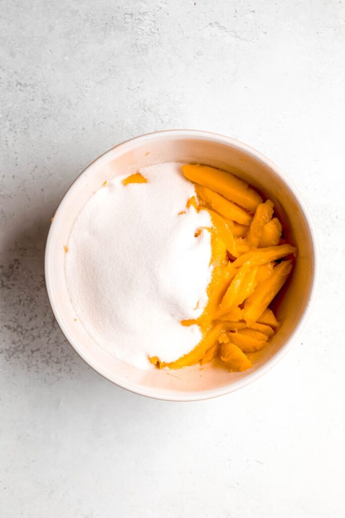 mango slices, lemon juice, and sugar added to a bowl. 